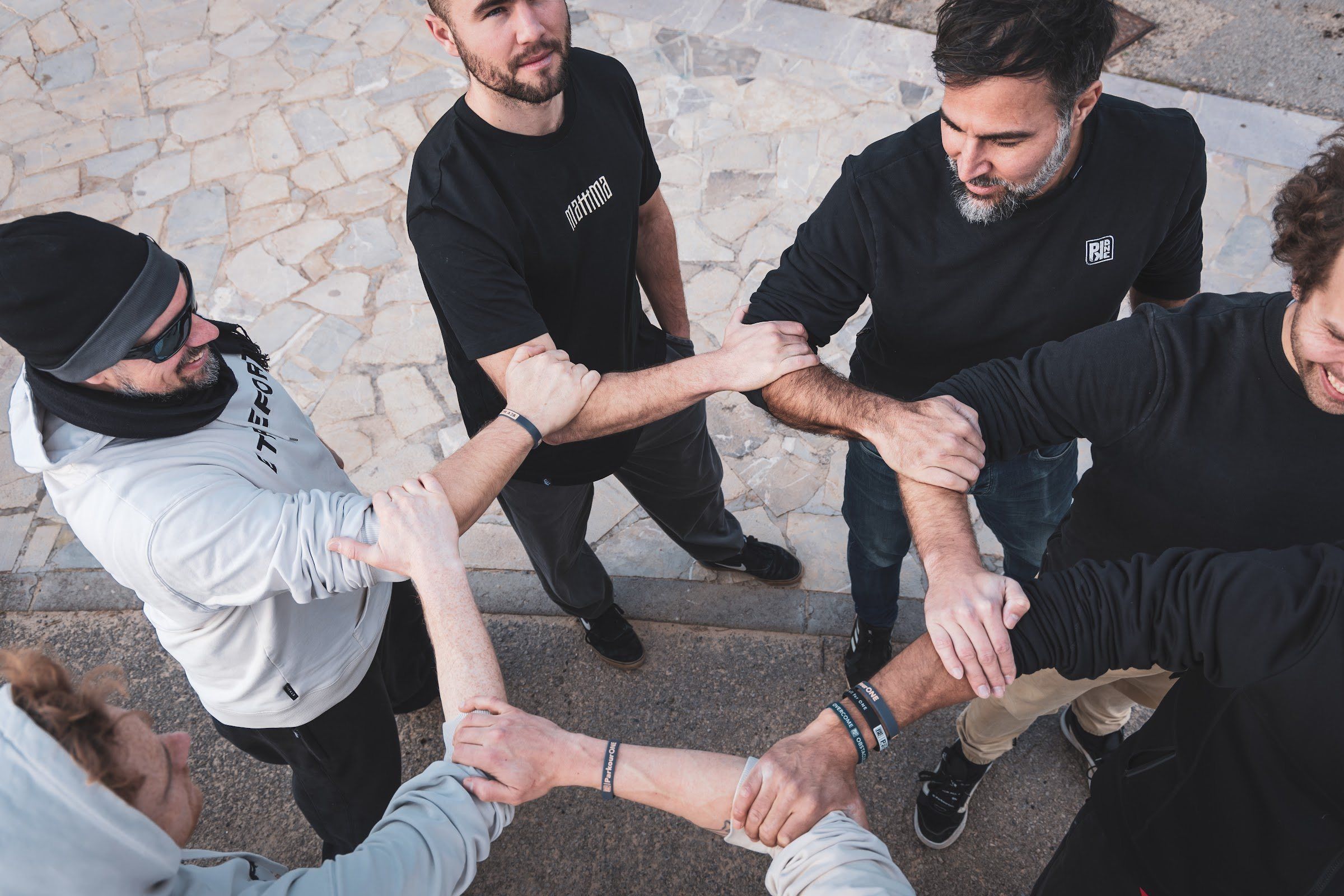 Seen from above, a group of men stand in a circle gripping each other's forearms.
